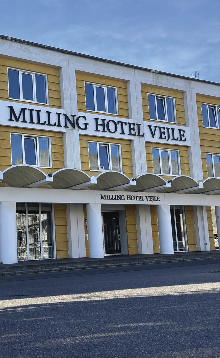 A yellow and white hotel with a blue sign in front. Description generated by AI